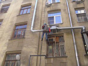 kiipeilijä asentaa ilmanvaihtokoneen rakennuksen ulkopuolelle